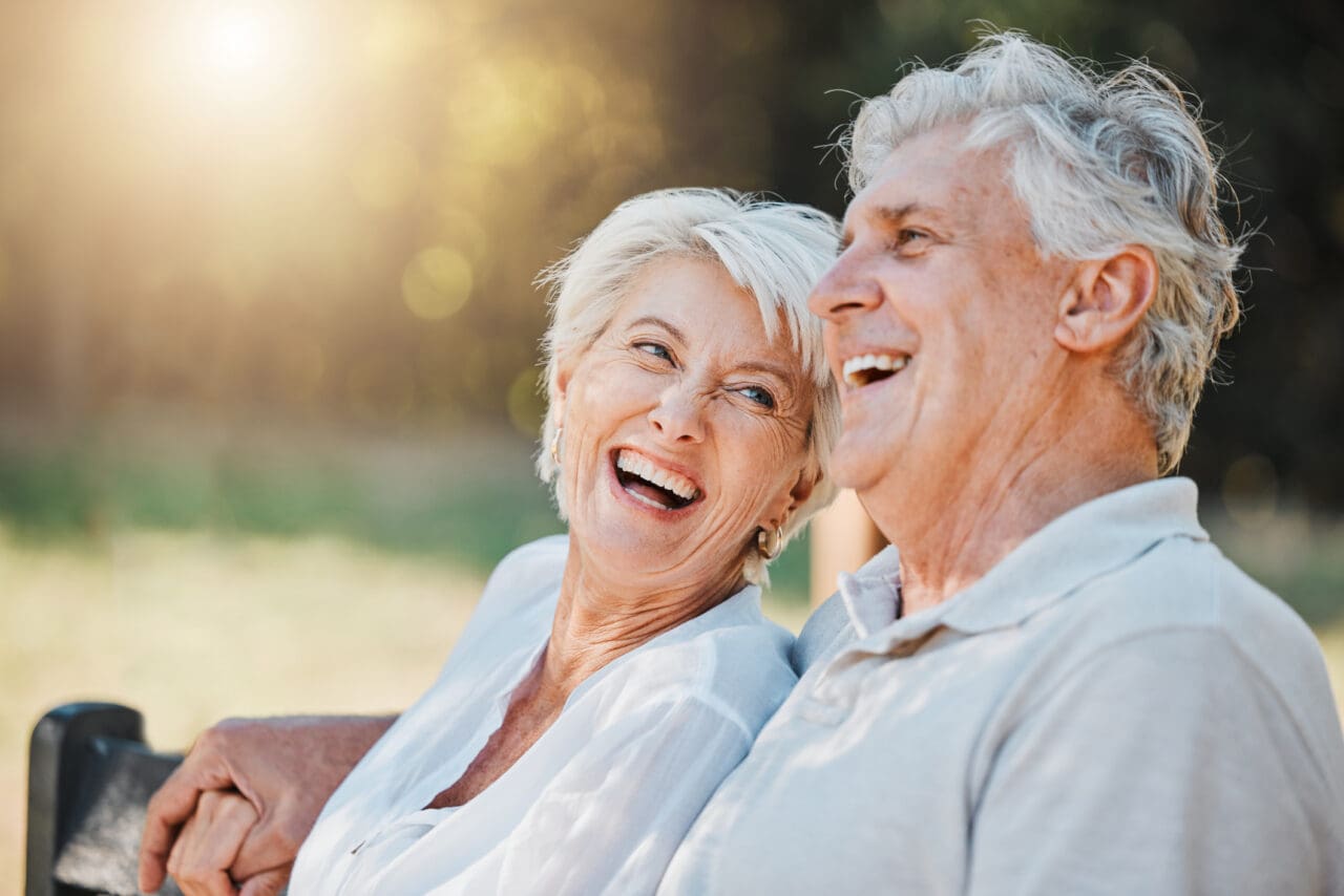 Senior couple, laughing or park bench in nature, happy with Medicare insurance